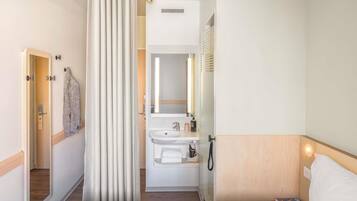 A hotel room with a bed, a bathroom with a sink and mirror, and a shower curtain.