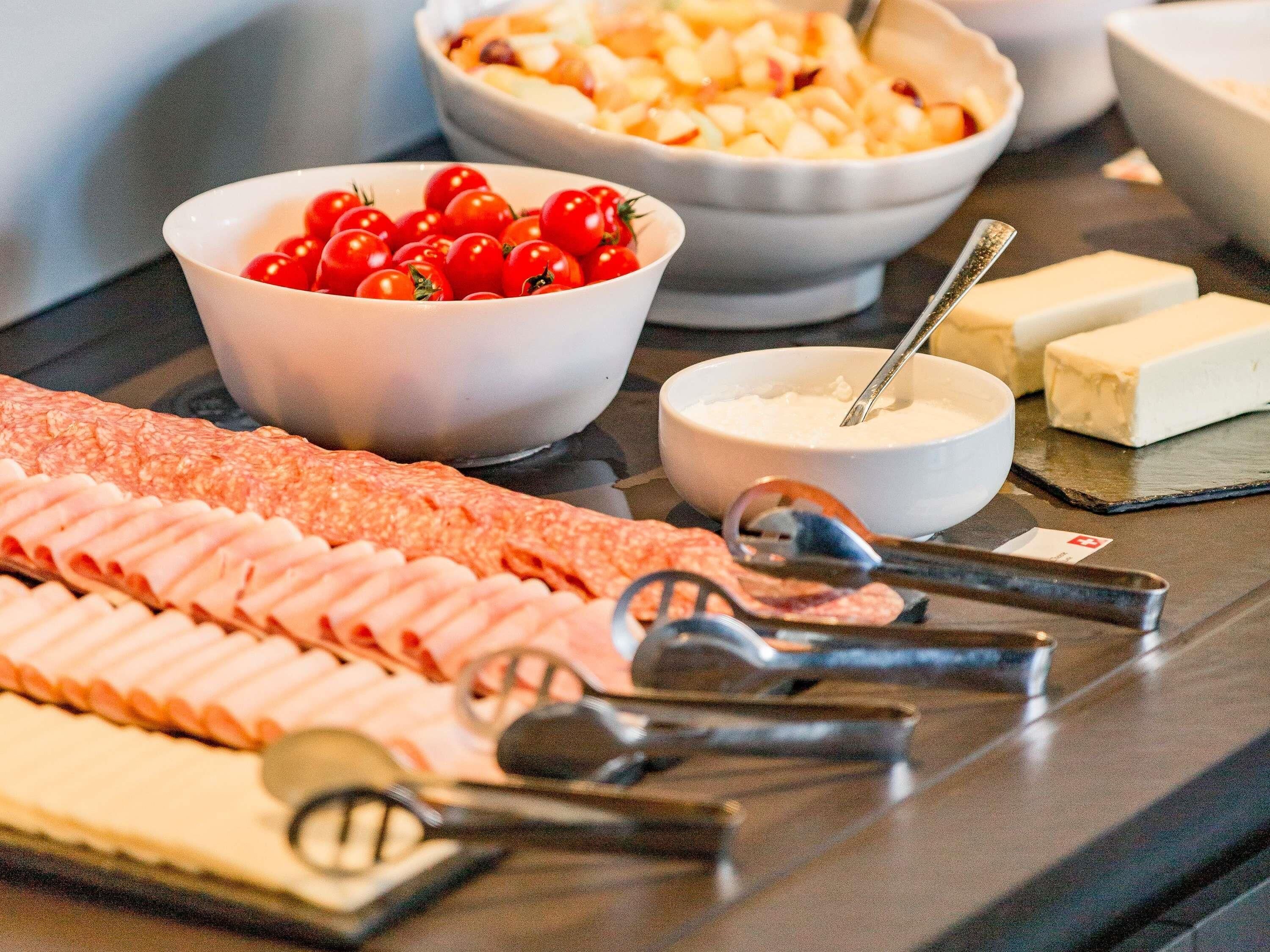 A buffet with various food items including a selection of meats, a bowl of cherry tomatoes, and a bowl of soup.