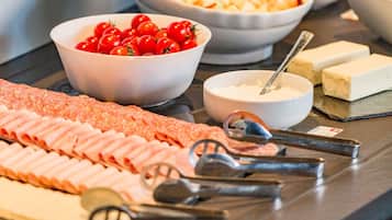 A buffet with various food items including a selection of meats, a bowl of cherry tomatoes, and a bowl of soup.