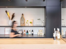 Una zona de bar con mostrador, botellas de vino, copas y objetos decorativos en estantes.
