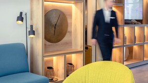 Eine moderne Lobby mit einem blauen Sofa, einem gelben Sessel, einer großen Wanduhr und einem Fernseher.