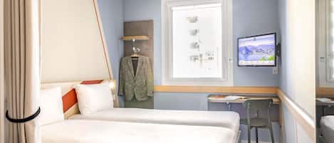 Habitación de hotel con cama, escritorio, silla, televisión y ventana con vista a edificios.