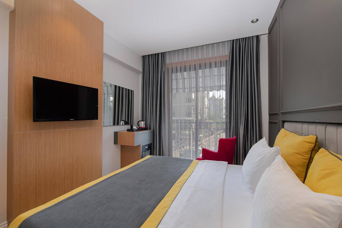 Une chambre d’hôtel moderne dotée d’un grand lit, d’un téléviseur à écran plat fixé au mur, d’un bureau avec une chaise et offrant une vue sur la ville grâce à de grandes fenêtres.