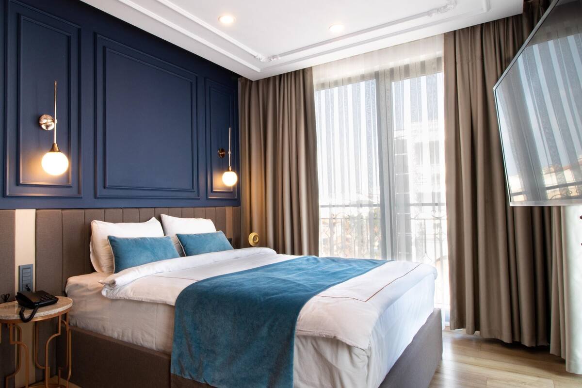 Une chambre d’hôtel moderne avec un grand lit, une table de chevet et une vue sur la ville grâce à de grandes fenêtres.