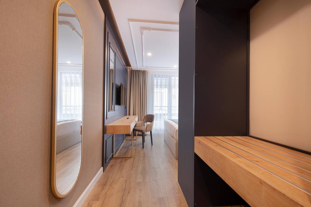 Une chambre d’hôtel moderne avec un bureau en bois, une chaise, un grand miroir et un banc.