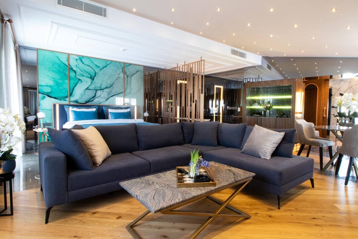 Un salon moderne avec un canapé d’angle bleu foncé, une table basse en verre et un plancher en bois.