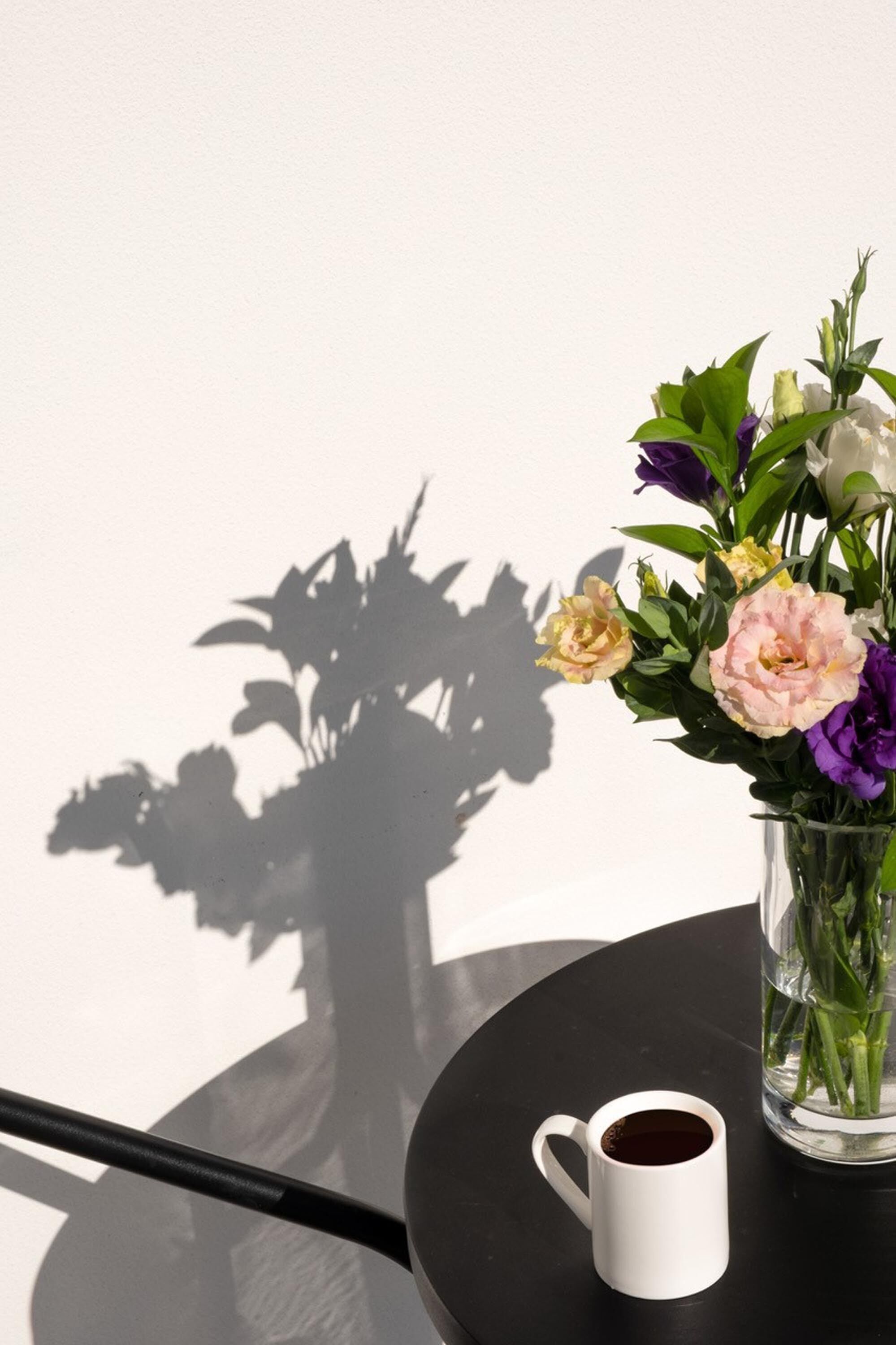 Una taza blanca sobre una mesa redonda con un florero de vidrio transparente con flores.