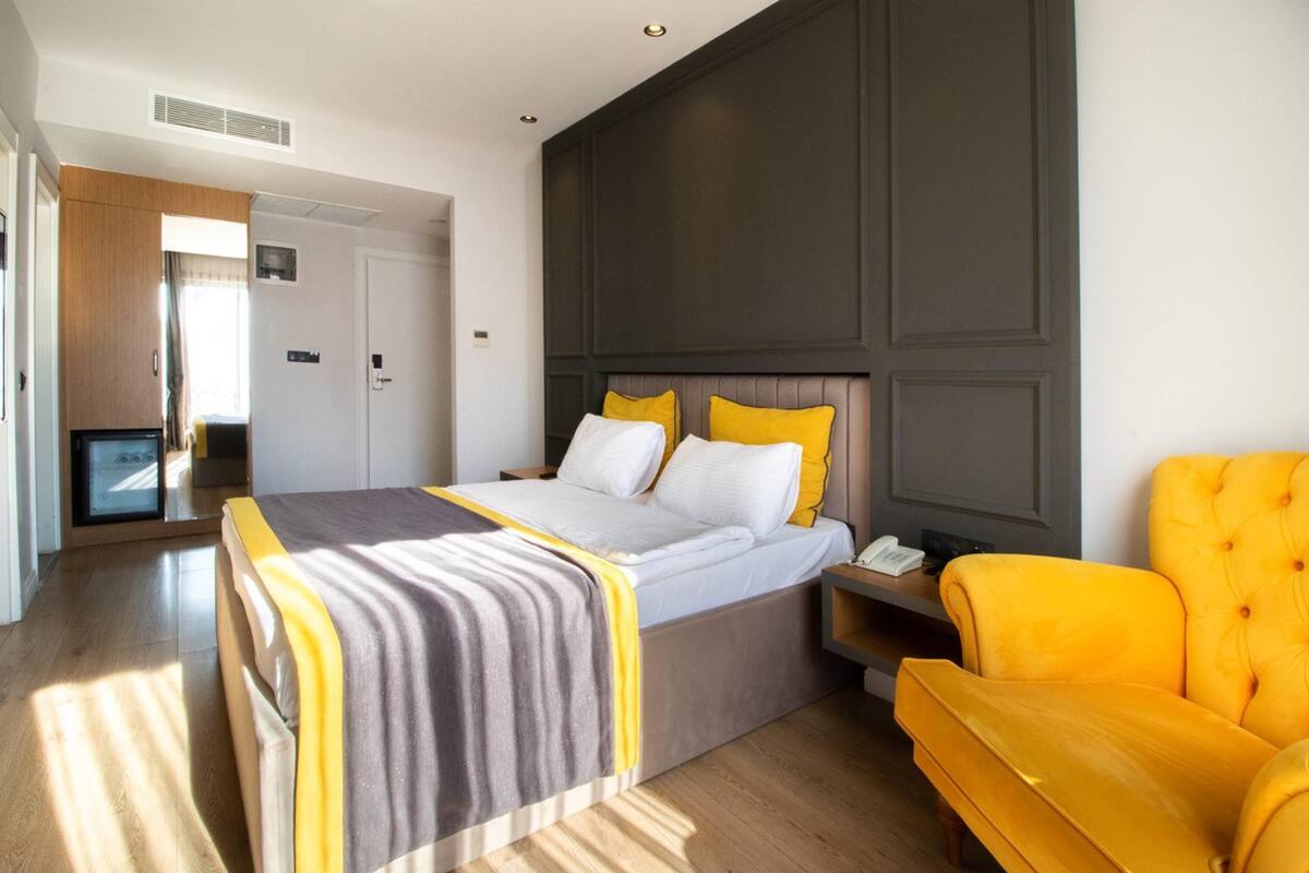 Une chambre d’hôtel avec un lit, une télévision, un fauteuil jaune et une table de chevet.