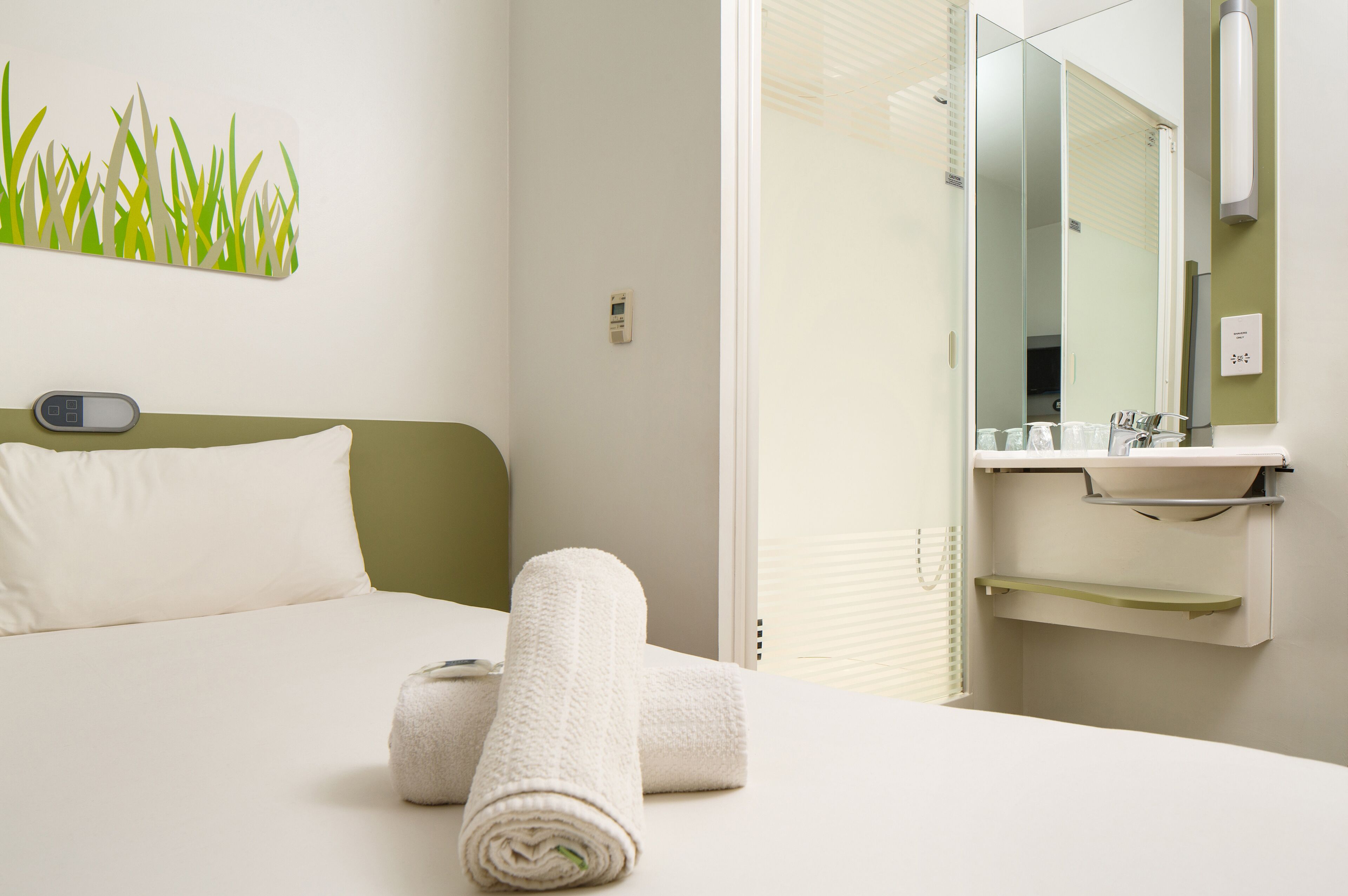 Una habitación de hotel con una cama, una mesita de noche, un espejo y una toalla sobre la cama.