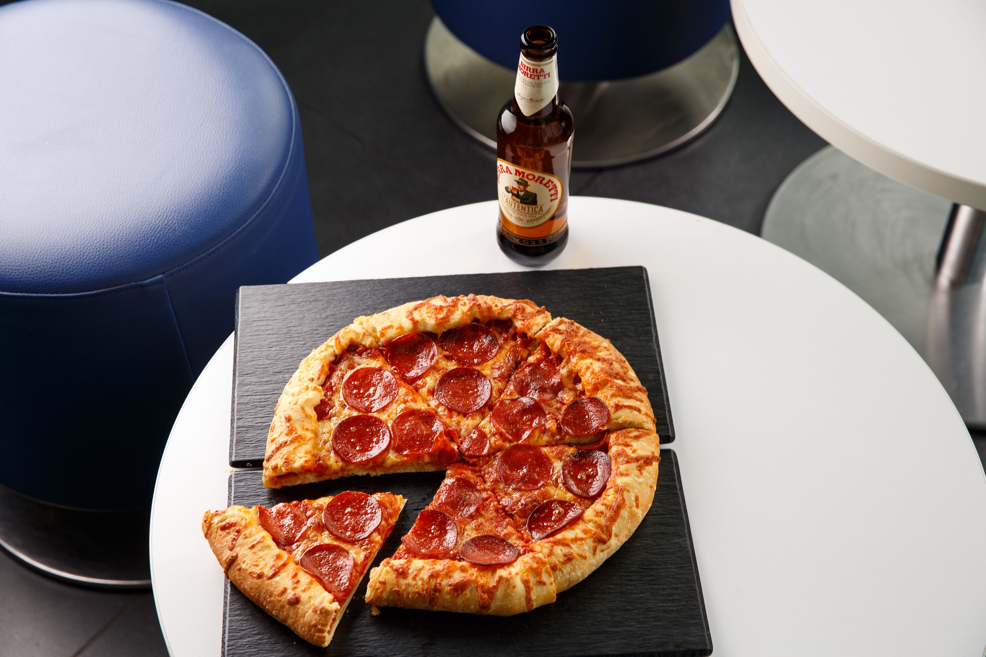 Una pizza sobre una tabla de pizarra negra, con una botella de cerveza al fondo.