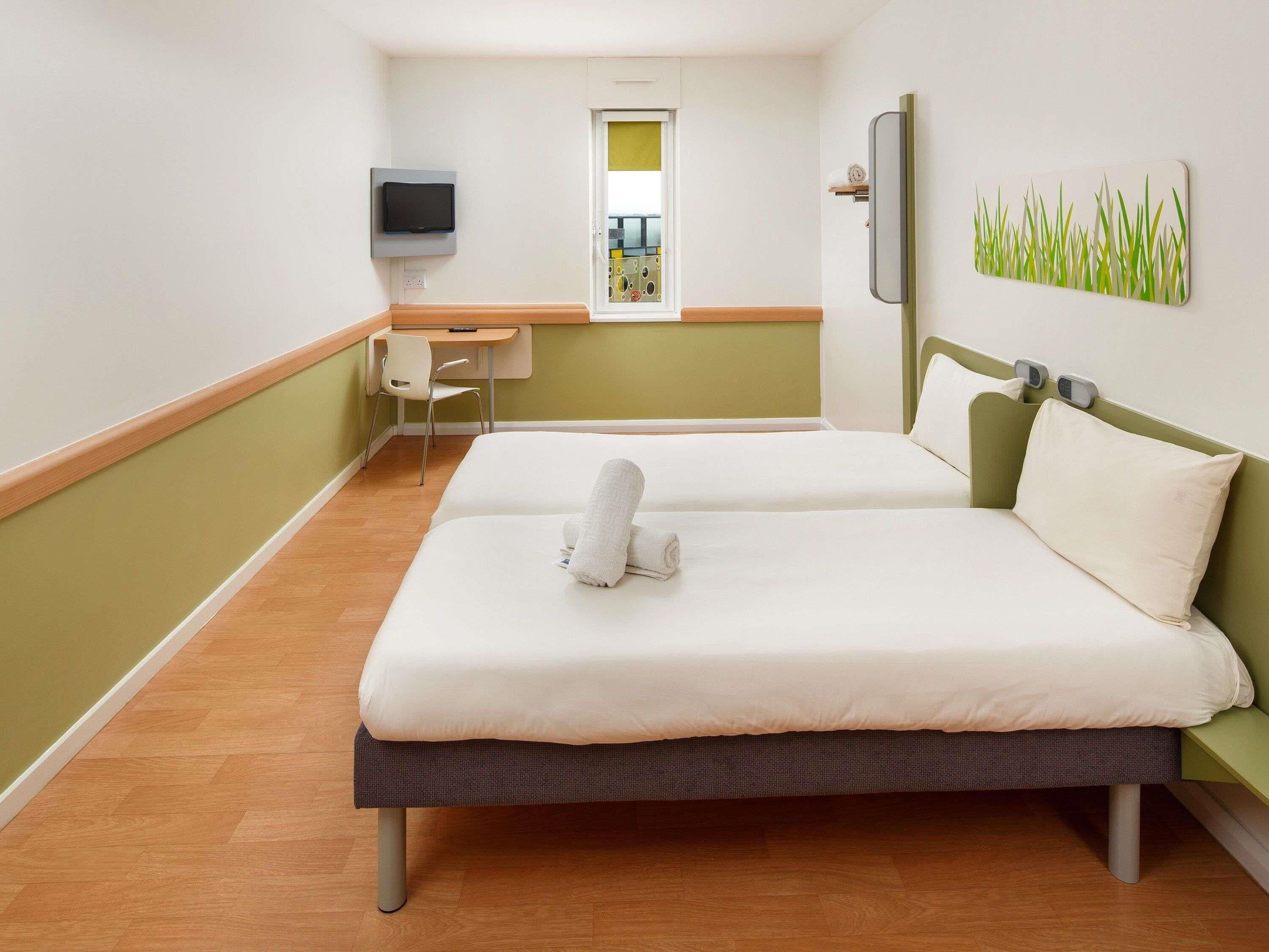 Une chambre d’hôtel avec deux lits, un bureau, une télévision et une œuvre d’art accrochée au mur.