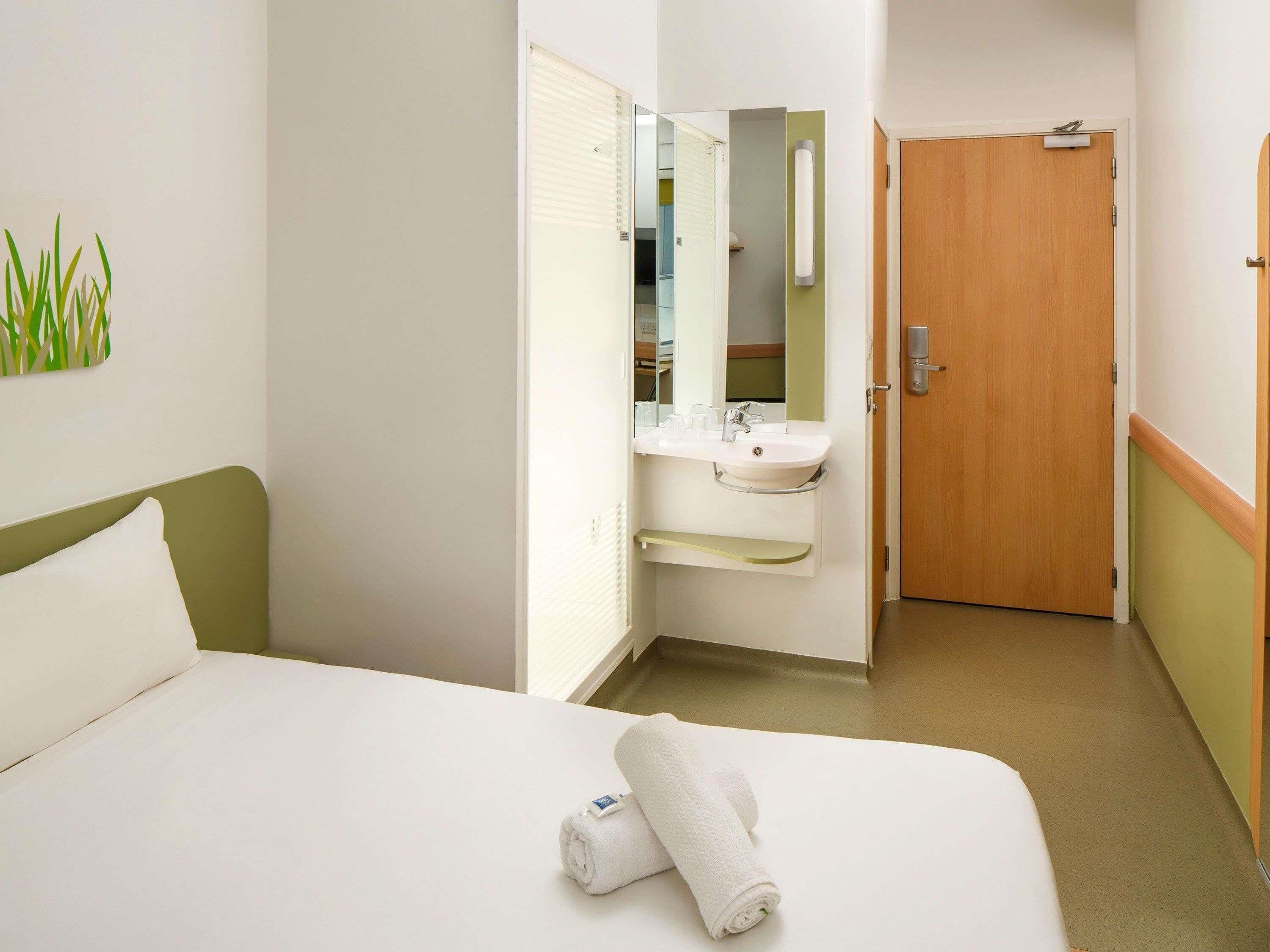 Habitació d'hotel amb un llit, un bany amb un rentapins i un mirall, i una porta.