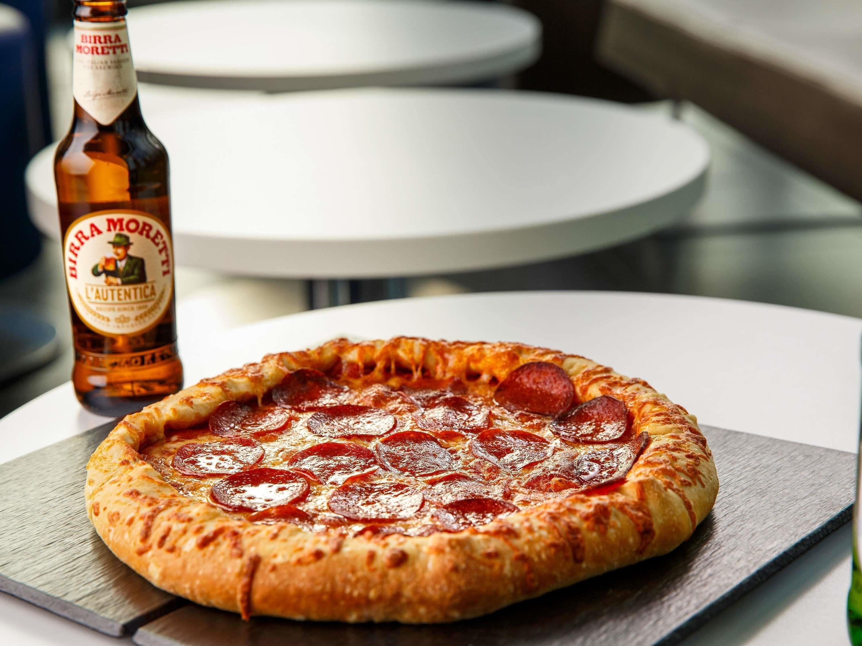 A pizza with pepperoni slices on a wooden board, a bottle of Birra Moretti beer, and white plates on a table.