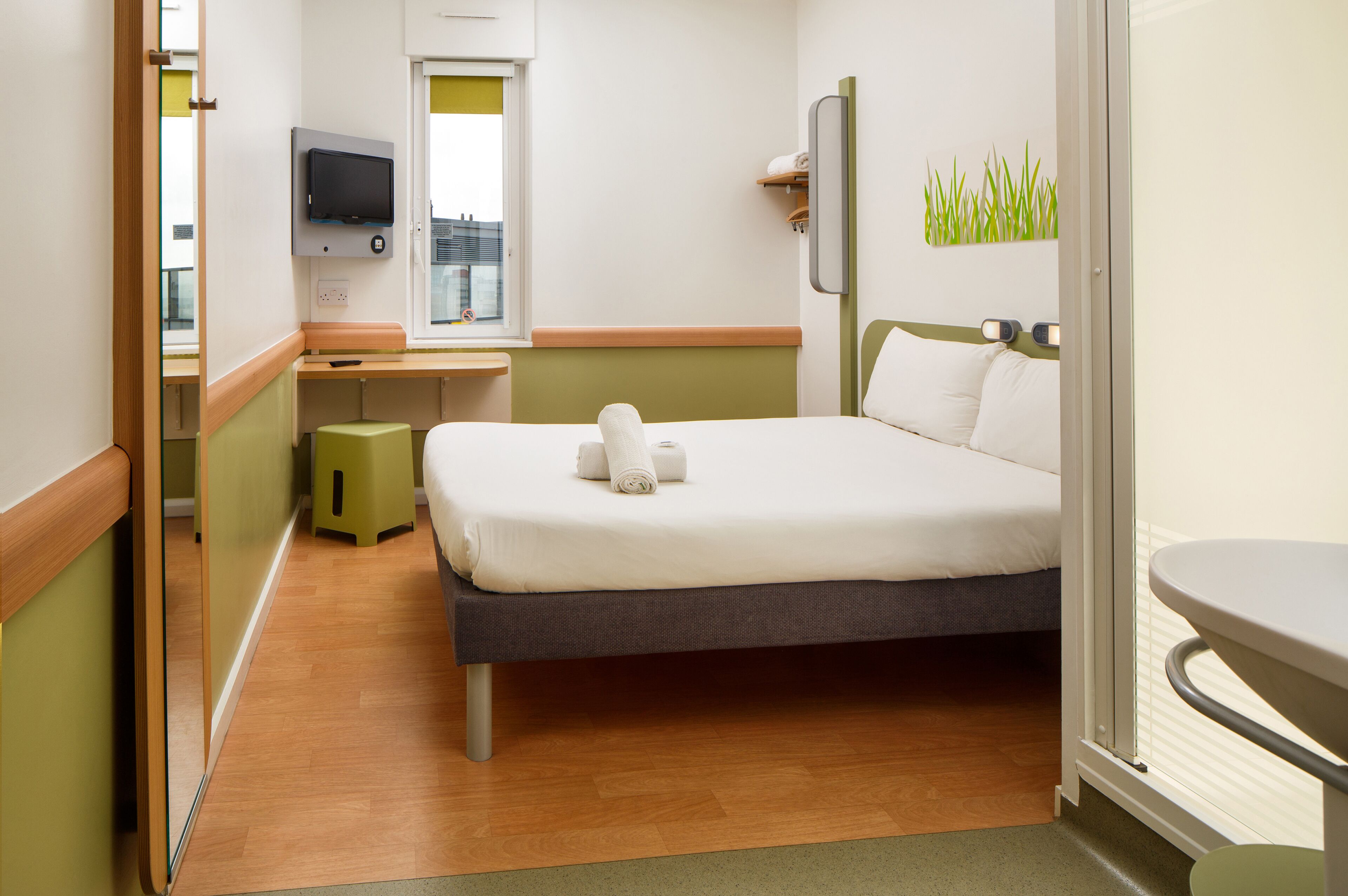 Una habitación de hotel con cama, televisión, un escritorio pequeño y ventana.