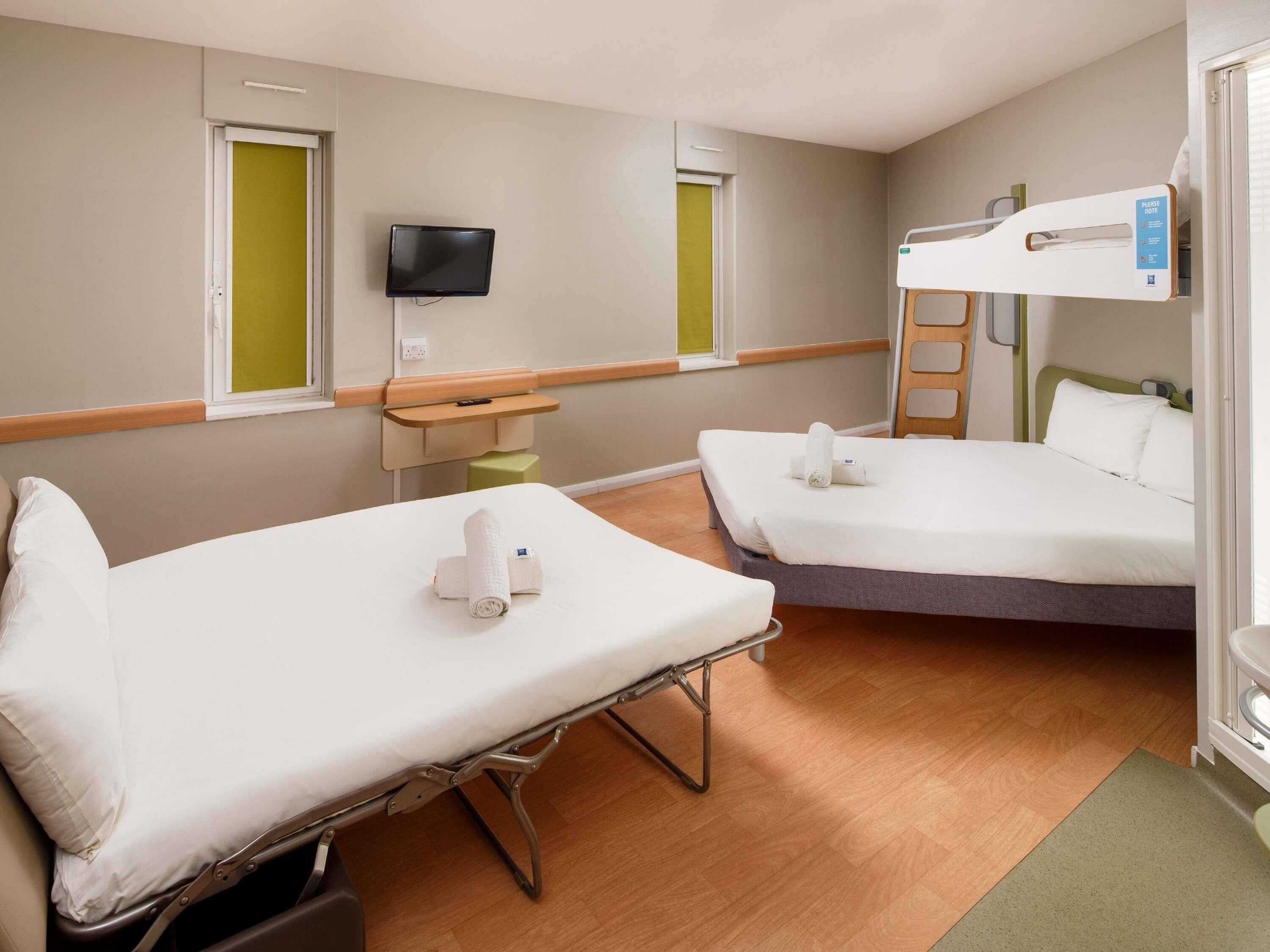 Une chambre d’hôtel avec deux lits, une télévision, un bureau et une fenêtre.