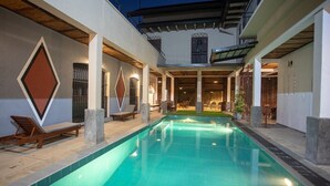 A swimming pool with lounge chairs and a covered area with tables and chairs. - Serenity Lake Front Villa (Moratuwa)
