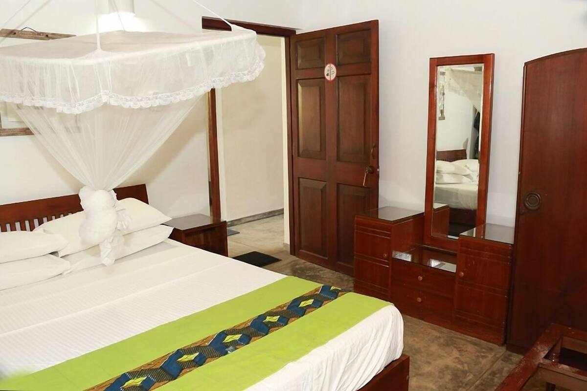 A hotel room with a bed, a wooden wardrobe, a mirror, and a door.