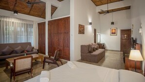 A hotel room with a bed, a sofa, a dining table, and a chair. There are wooden doors and a ceiling fan. - Serenity Lake Front Villa (Moratuwa)