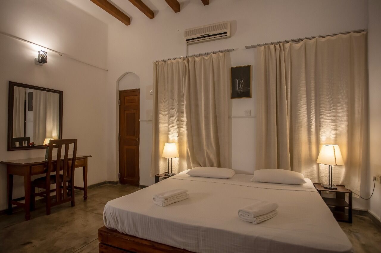 Une chambre d’hôtel comprenant un lit, deux lampes de chevet, un bureau avec une chaise, un miroir et une porte.