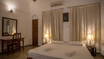 Une chambre d’hôtel comprenant un lit, deux lampes de chevet, un bureau avec une chaise, un miroir et une porte.