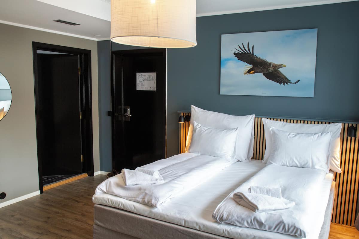 Habitación de hotel con una cama grande, una lámpara de techo, un cuadro de un águila y una puerta con un aviso.