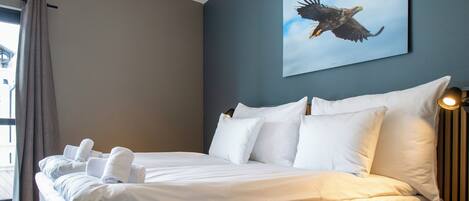 A double bed with white linens and pillows, a large window with curtains, and a wall-mounted picture of an eagle.