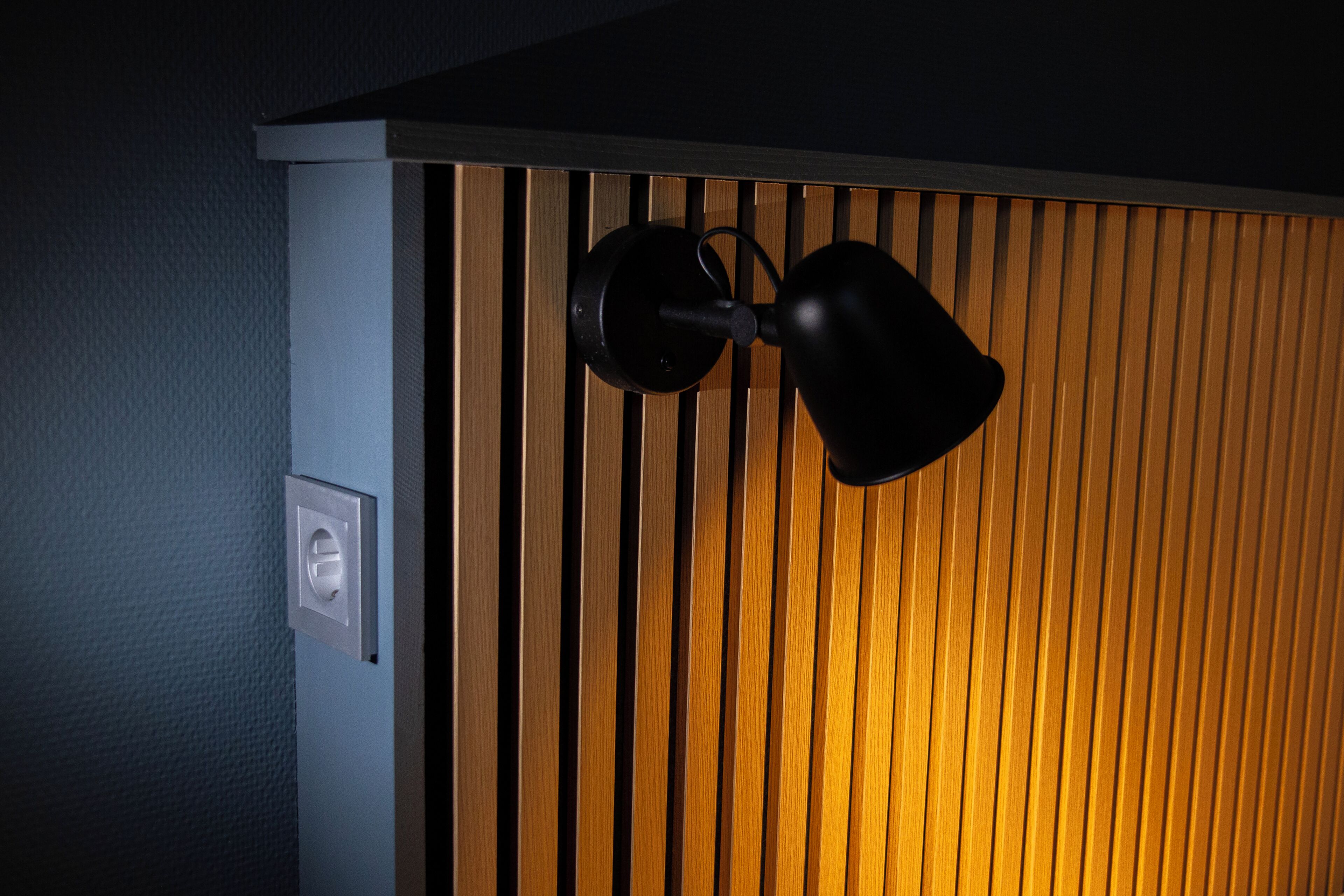 A wall with vertical wooden slats and a black wall-mounted light fixture.