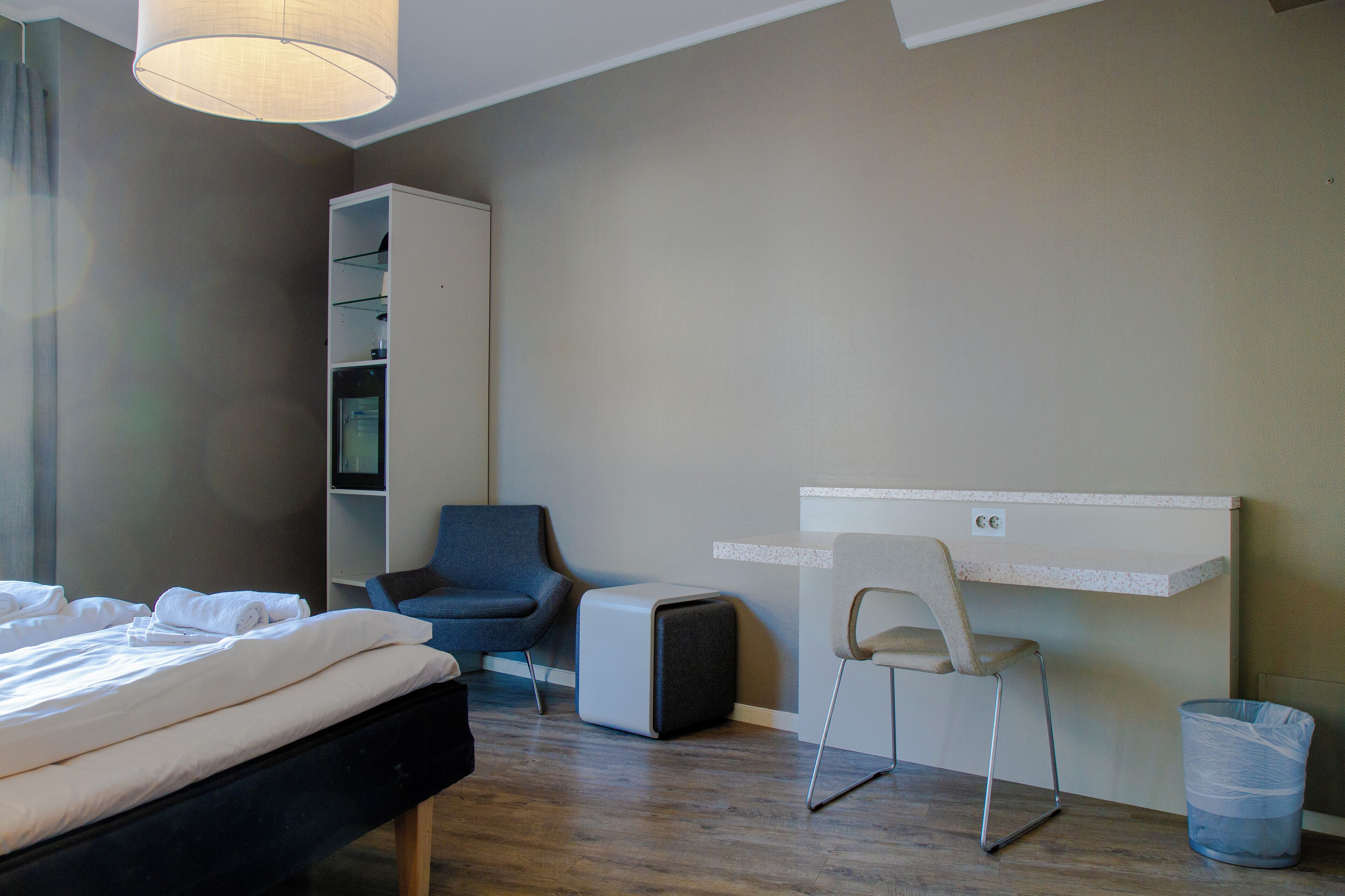 Ein Hotelzimmer mit Bett, Schreibtisch, Stuhl, Kleiderschrank und Mülleimer.
