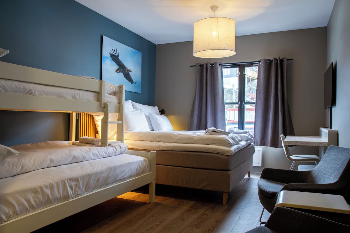 Habitación de hotel con literas, un escritorio, una silla, un ventanal con cortinas y un cuadro en la pared.