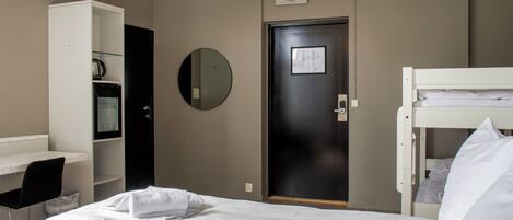 A hotel room with a bed, a desk, a chair, a wardrobe, and a door.