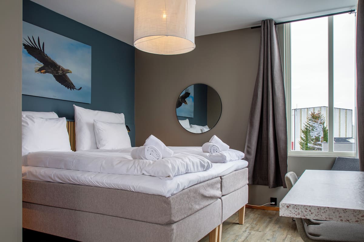 Habitación de hotel moderna con una cama grande, un espejo redondo y vistas a un paisaje nevado por la ventana.