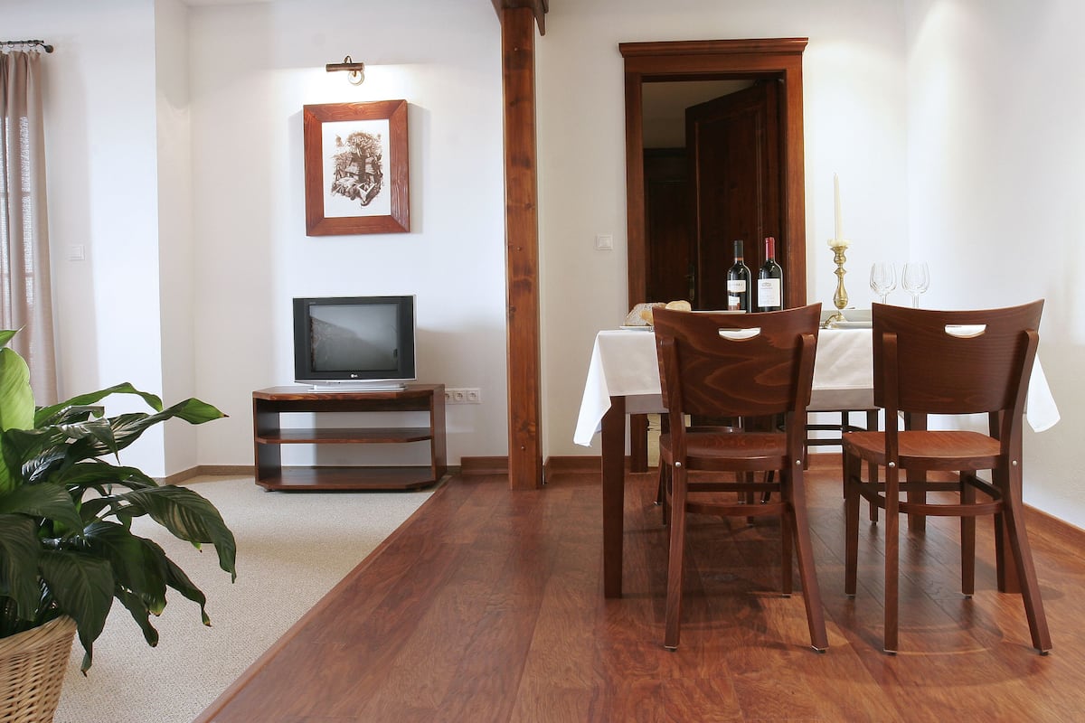 A dining area with a wooden table, chairs, a television on a stand, and a framed picture on the wall.
