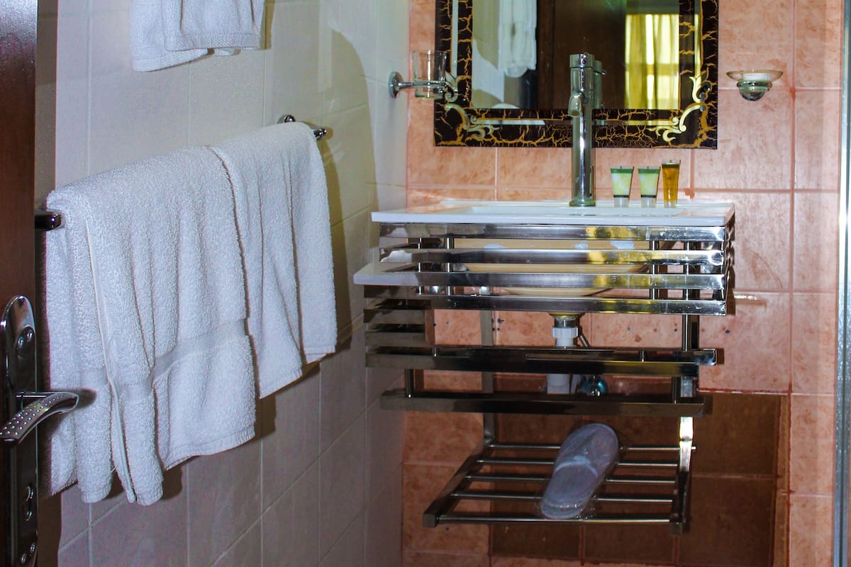 Une salle de bain avec un porte-serviettes blanc, un miroir avec un cadre doré et un lavabo avec un robinet chromé.