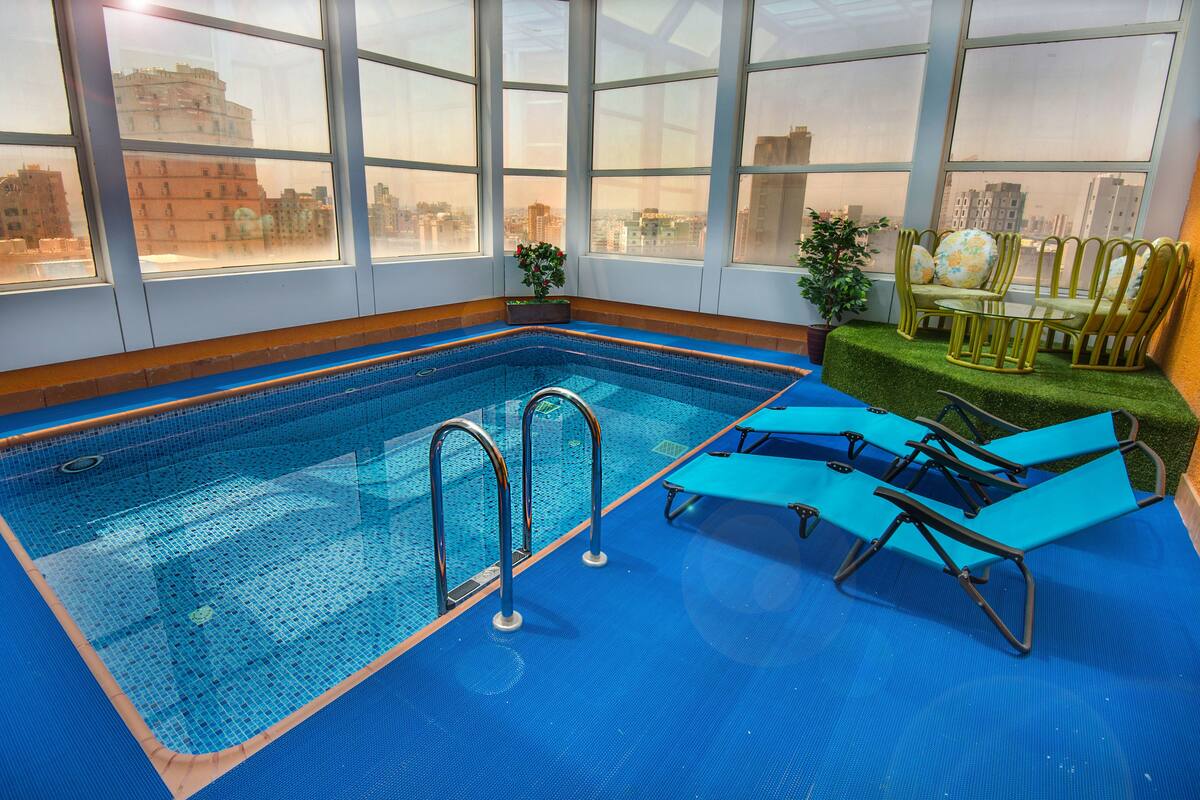 Une piscine intérieure à l’eau d’un bleu cristallin, entourée de grandes baies vitrées offrant une vue sur la ville.