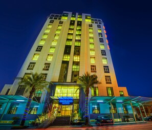 A tall hotel with multiple floors, a well-lit entrance, and a visible sign for the Bravo Royal Hotel. - Bravo Royal Hotel Suite (Salmiya)