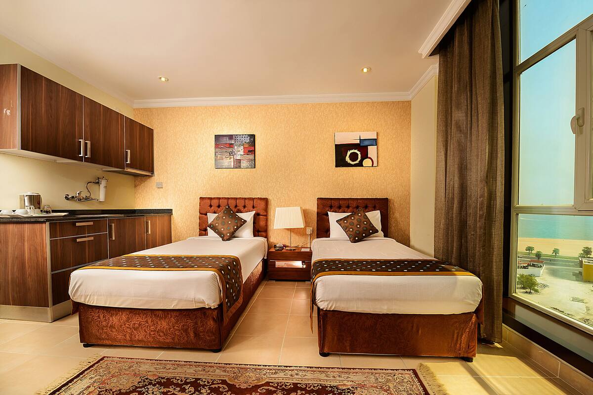 Une chambre d’hôtel avec deux lits, une petite kitchenette, une grande fenêtre donnant sur un beau paysage et un tapis décoratif.