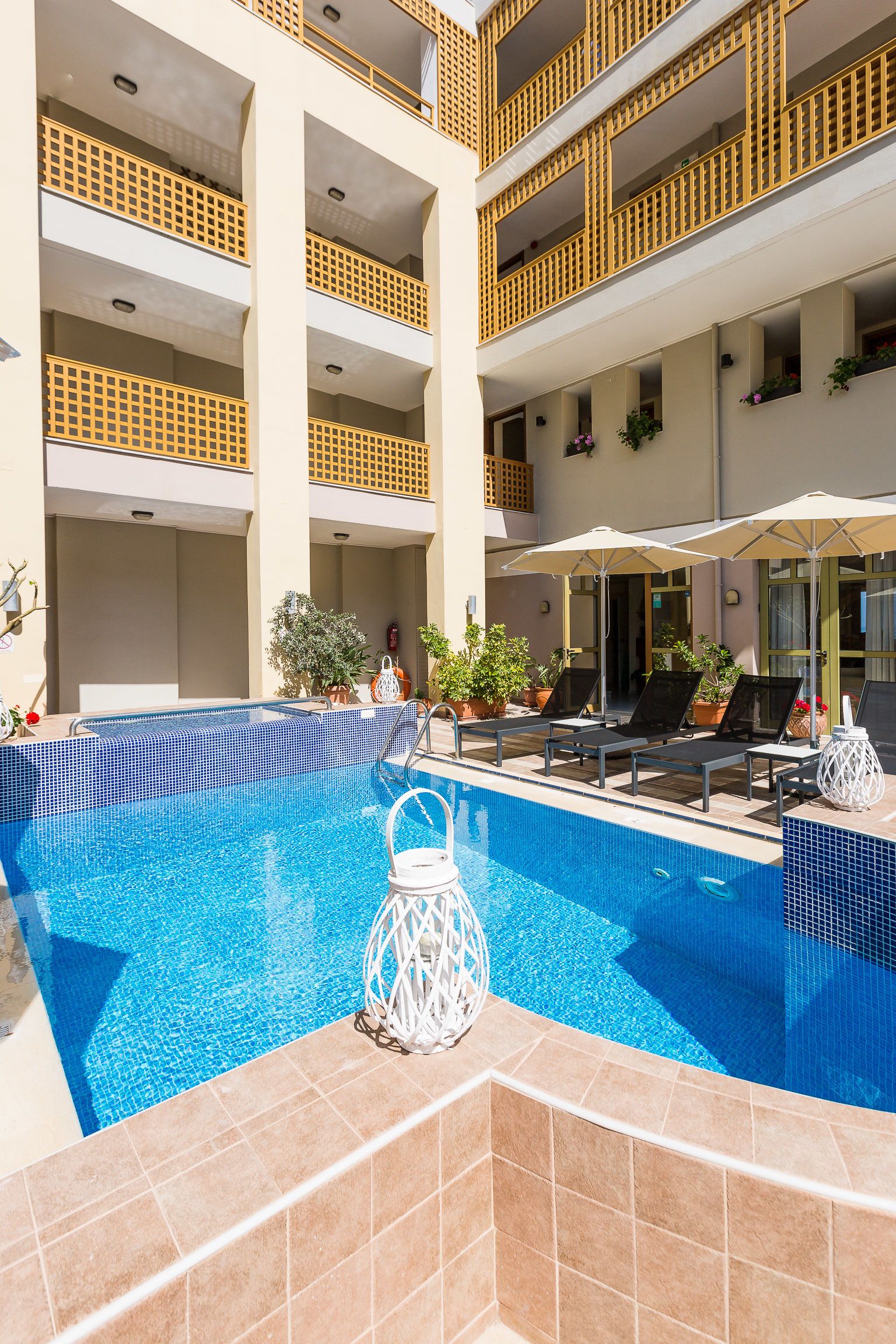 A pool area with lounge chairs and umbrellas, surrounded by balconies with yellow railings.