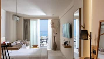A hotel room with a bed, a desk, a chair, a TV, and a view of the sea.