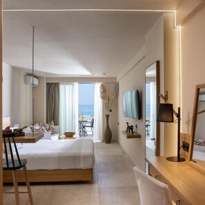 A hotel room with a bed, a desk, a chair, a TV, and a view of the sea. - Ammos Suites (Rethymno)