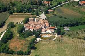Une vue aérienne d’un village rural avec des champs en terrasses, un bâtiment central doté d’une piscine et une route sinueuse.