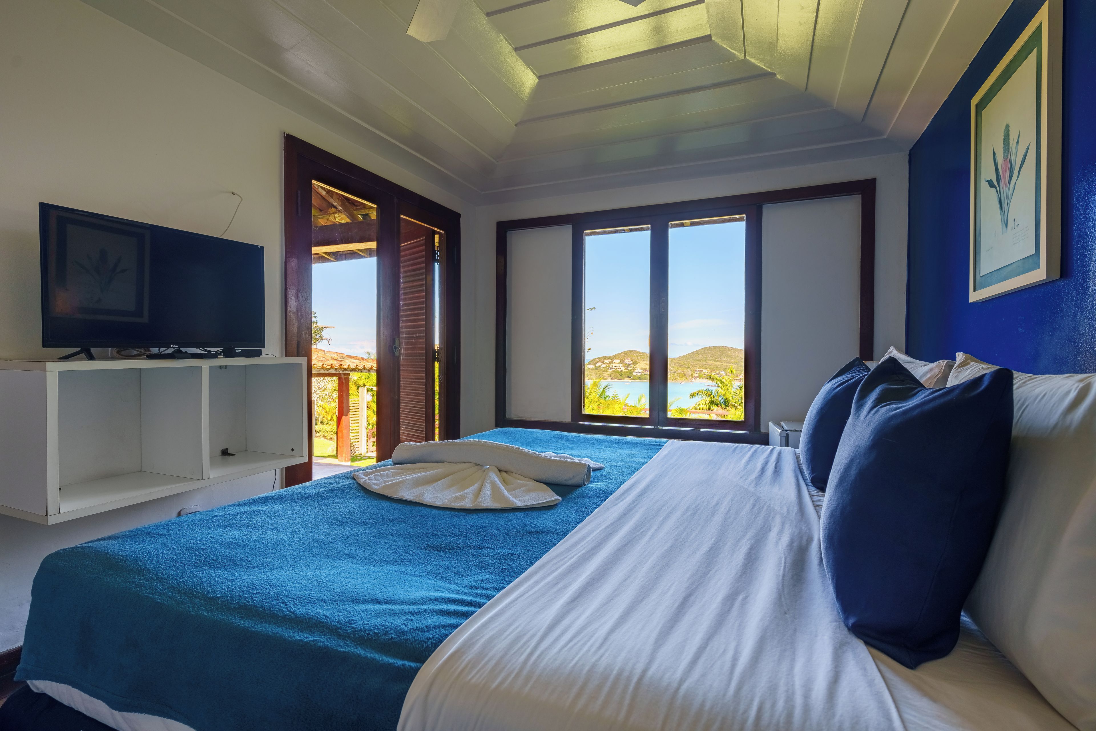A bedroom with a bed, a television, a window with a view, and a door.