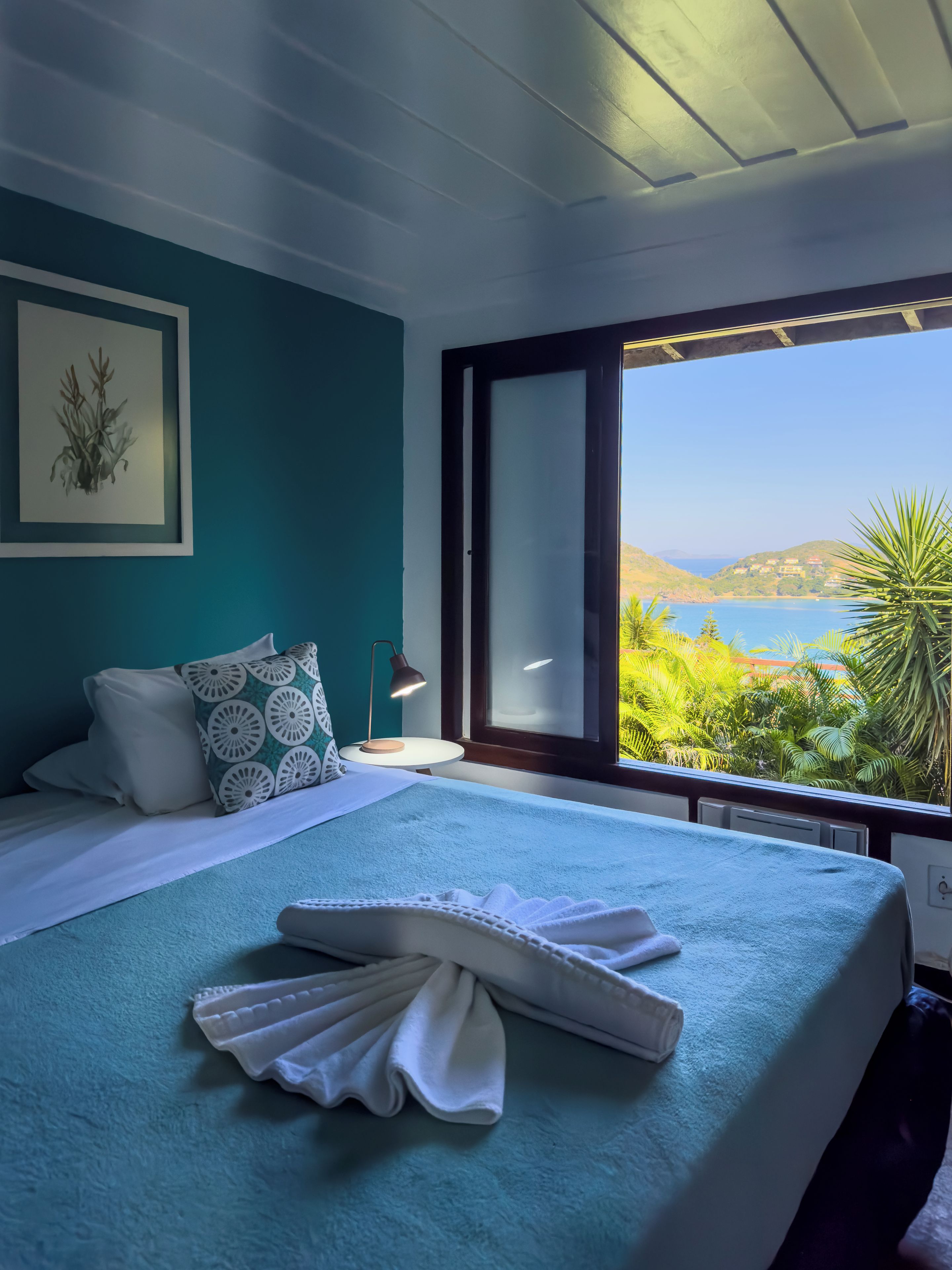Un dormitorio con cama, mesita de noche, lámpara y vistas a un paisaje costero.