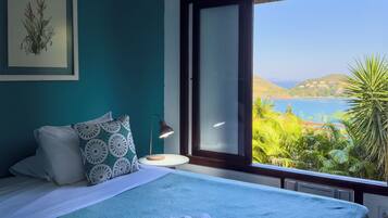 Un dormitorio con cama, mesita de noche, lámpara y vistas a un paisaje costero.