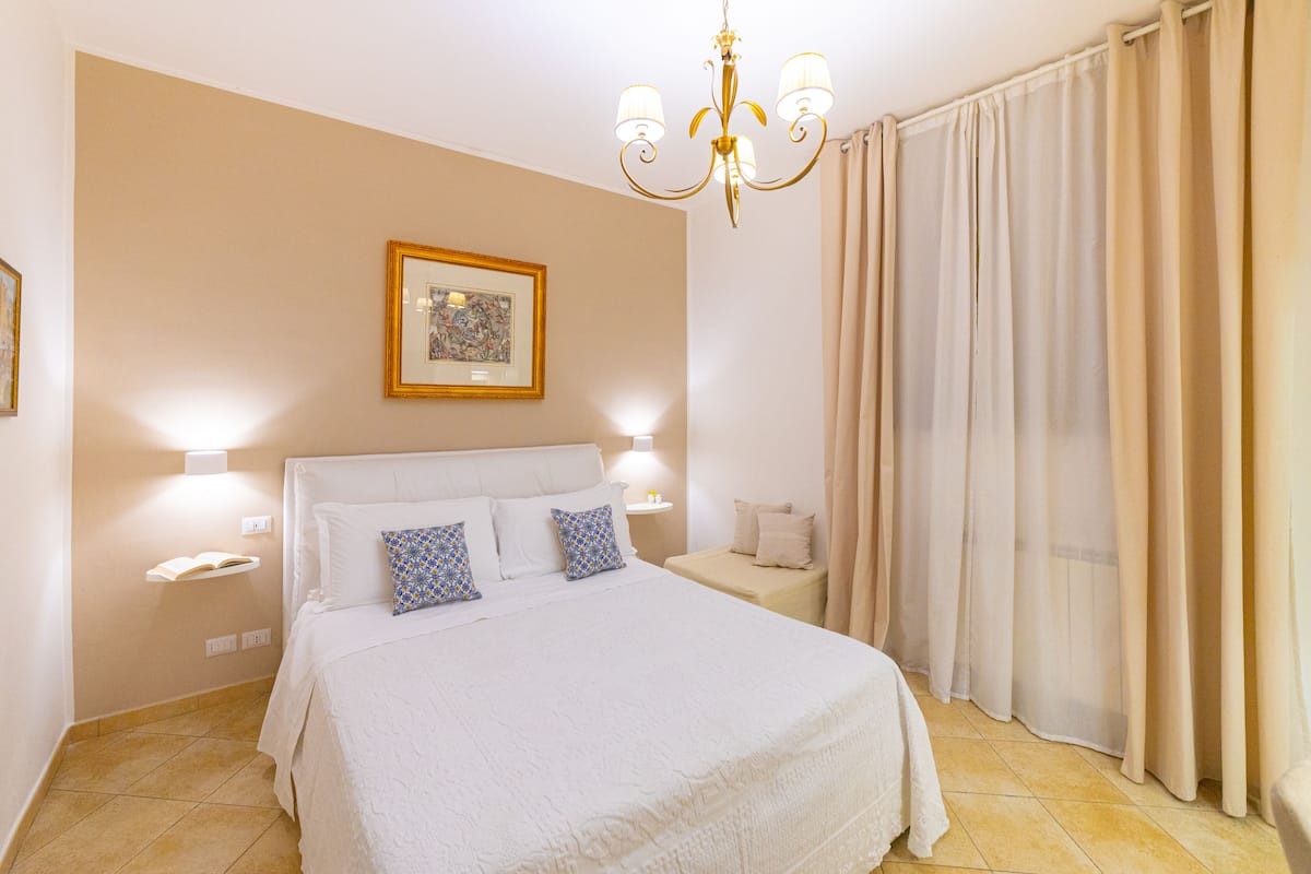 Un dormitorio ordenado con una cama grande, lámparas de noche, una mesita de noche, un cuadro en la pared y una araña.