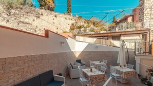 An outdoor patio with stone walls, wicker furniture, and tables with patterned tablecloths. - Bed and Breakfast Dionisio (Taormina)