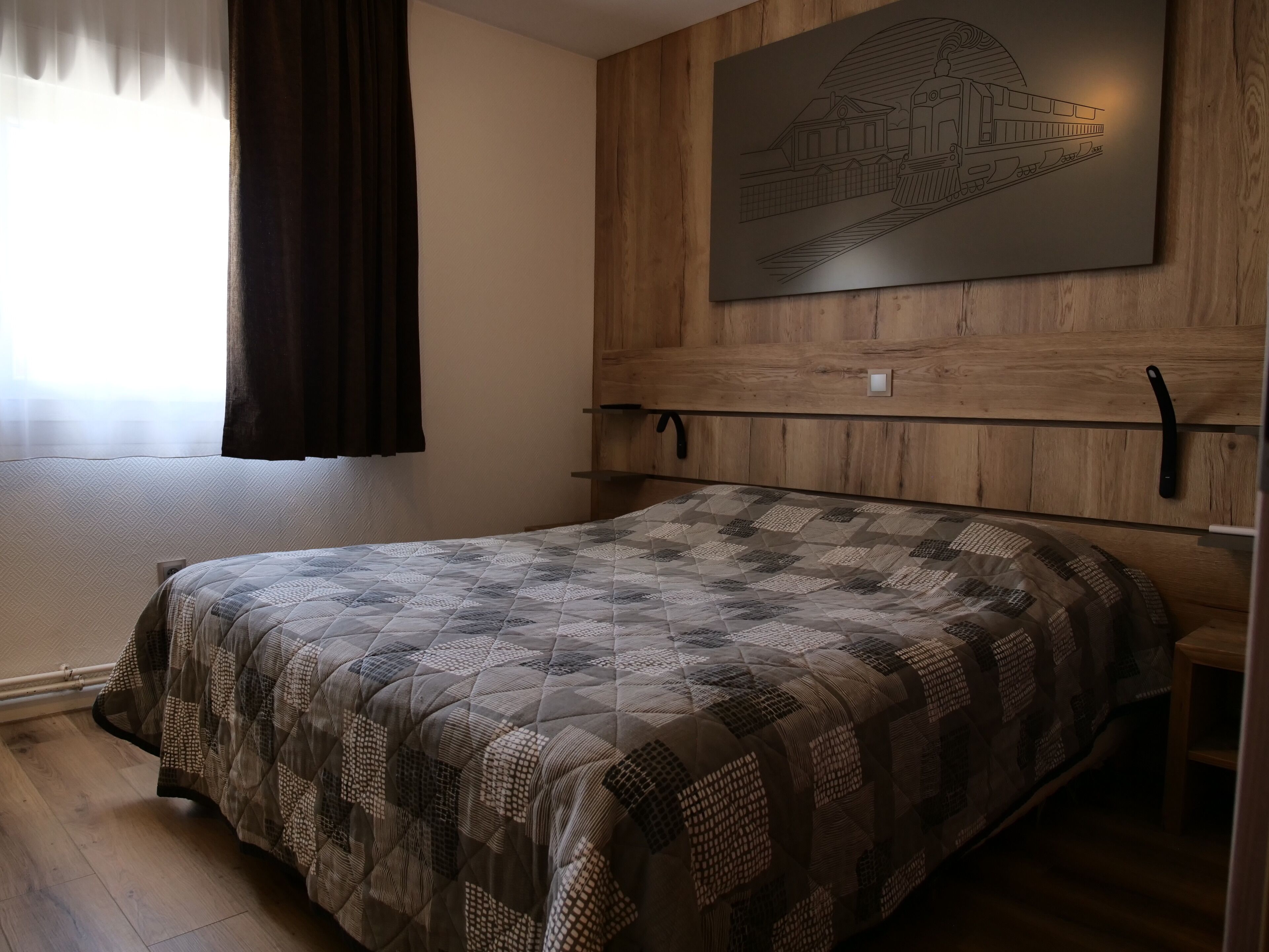 Ein Schlafzimmer mit einem hölzernen Kopfende, einer gesteppten Bettdecke und einem Wandbild einer Bahnhaltestelle.