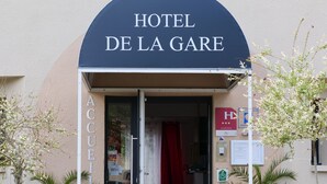 La entrada del Hotel De La Gare, con un porche cubierto, una puerta visible y plantas en macetas.