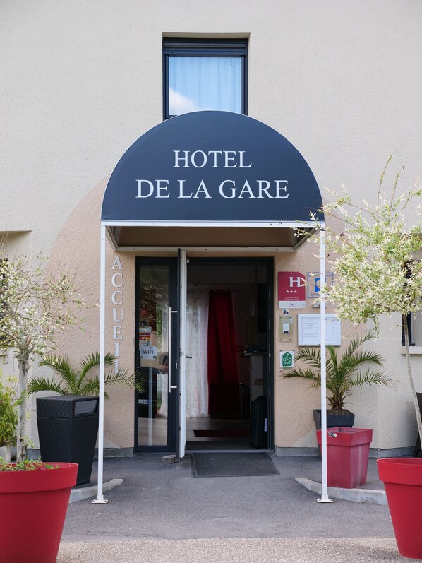 The entrance to Hotel De La Gare with a covered entrance, a visible door, and potted plants.