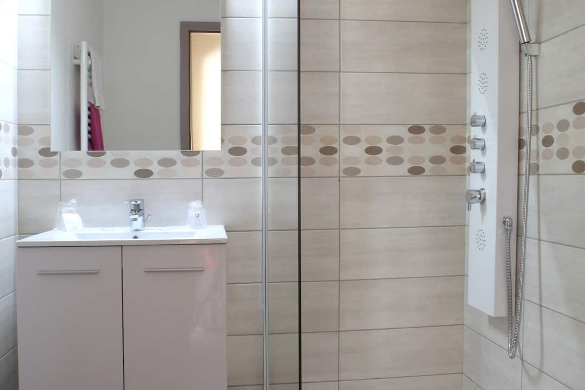 Un baño moderno con cabina de ducha de vidrio, un lavamanos blanco con espejo y azulejos con diseño.