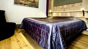 Un dormitorio con cama, una silla, suelo de madera y dos obras de arte en la pared que representan paisajes urbanos.